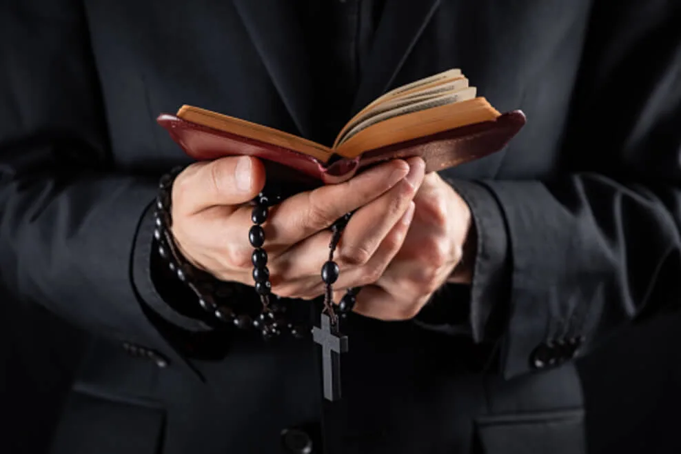 A priest or any religious person is holding a bible along with prayer beads
