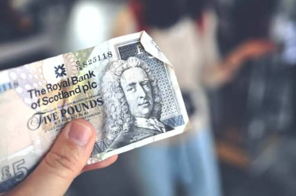 A person holding a note of five pounds