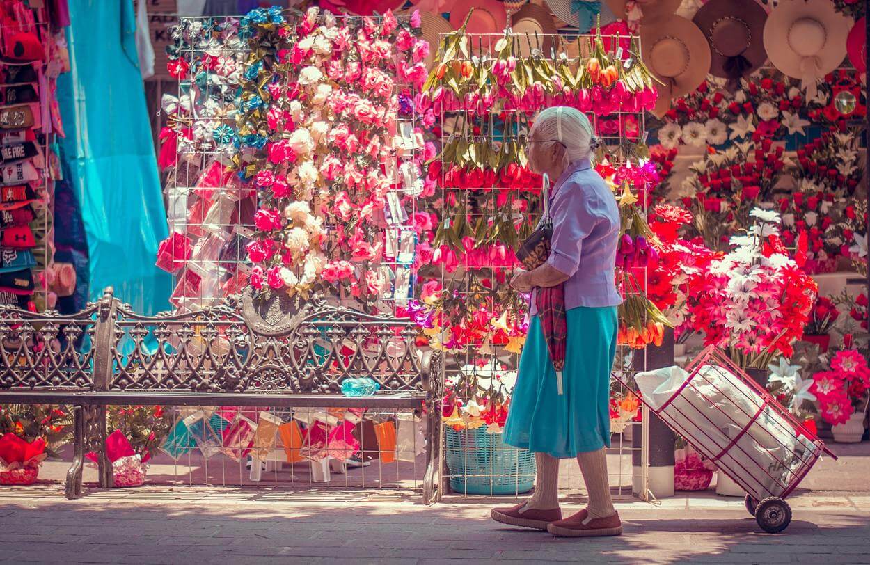An old woman walking past a flower shop. 
