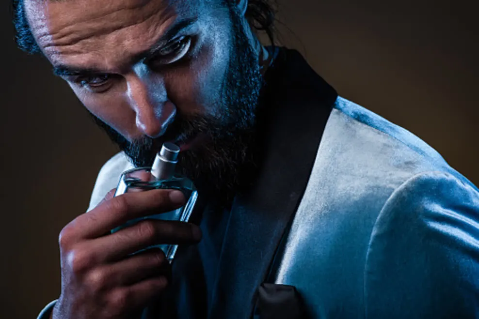 An image showing a masculine bearded man holding a bottle of perfume