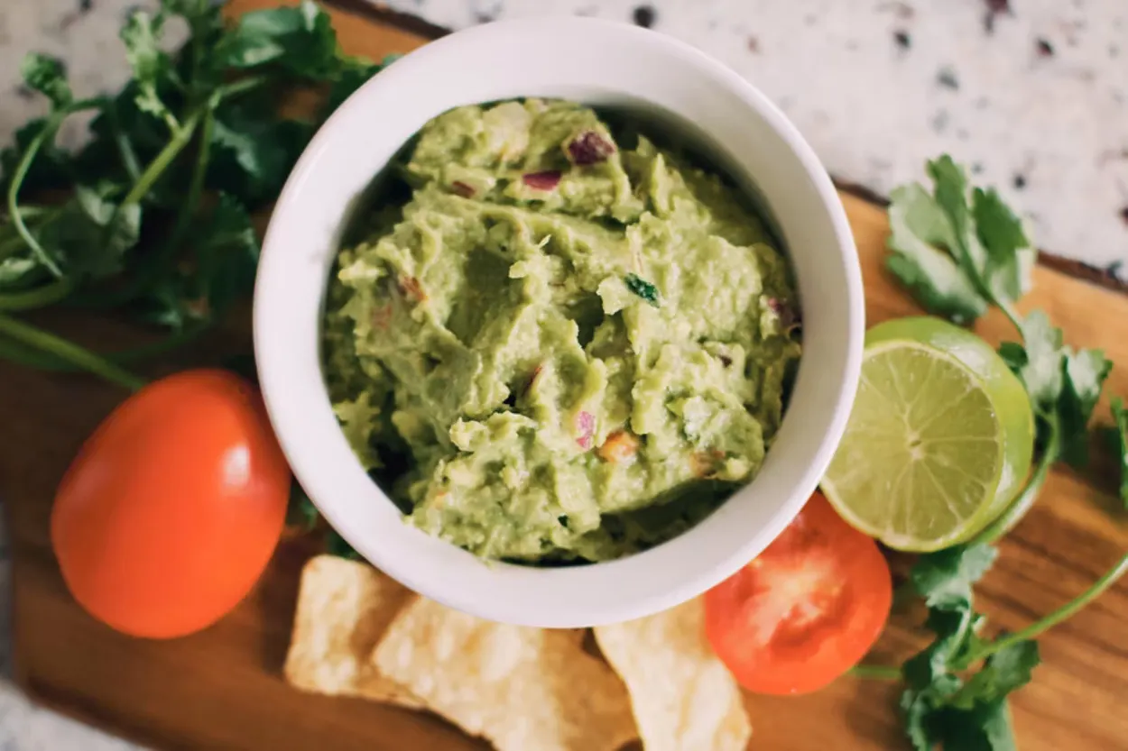A bowl of guacamole next to its main ingredients