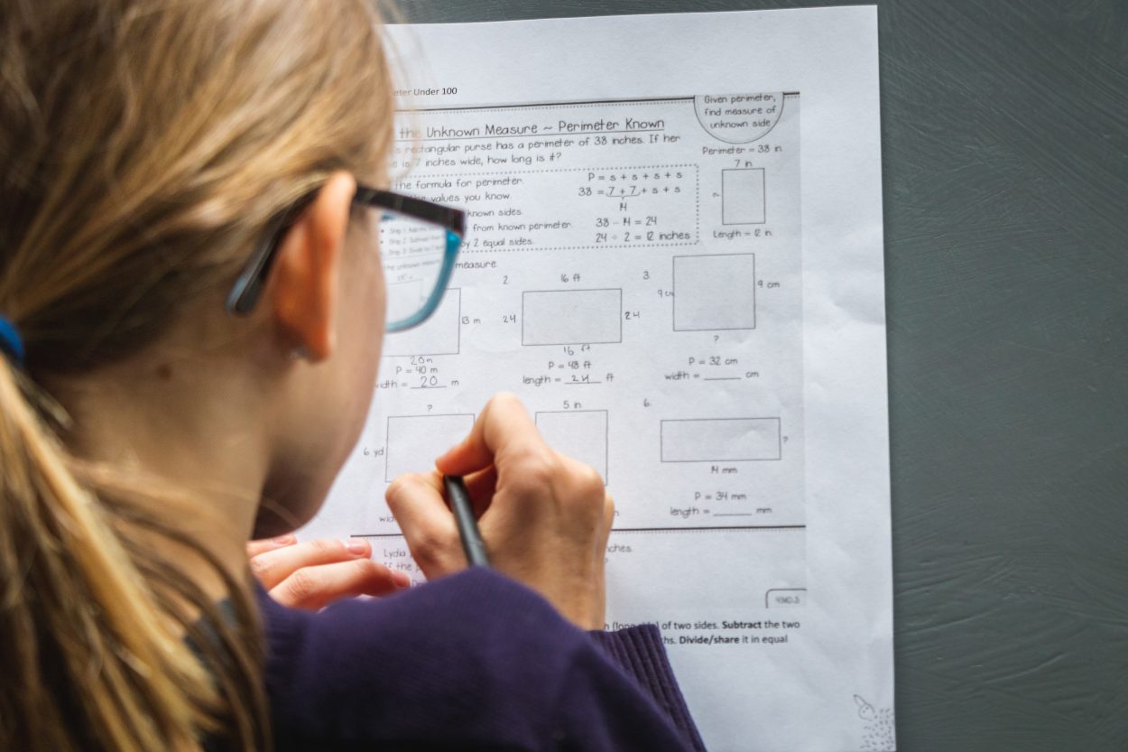 A girl with glasses solving a problem with a pencil in her hand.