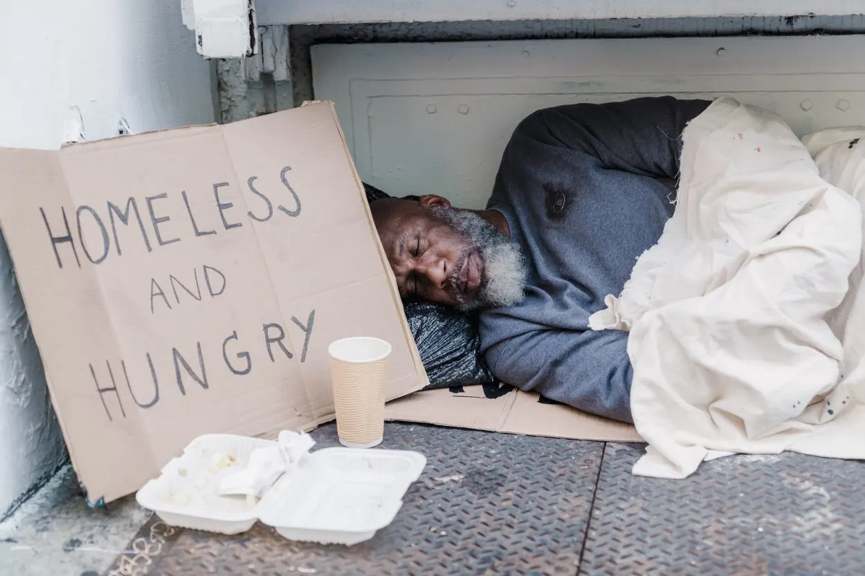A homeless person next to a cardboard sign