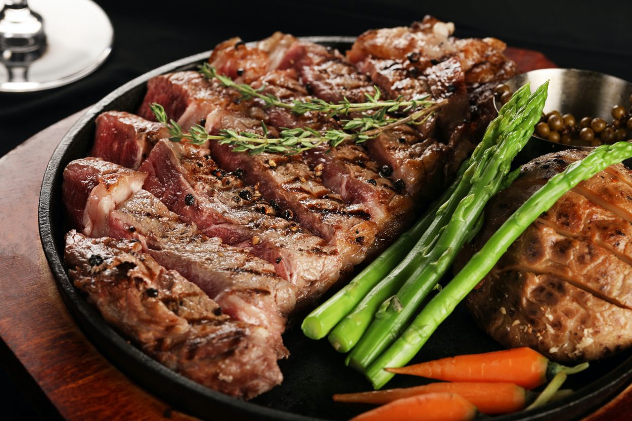 A platter that has a steak cut in strips with some vegetables on the side