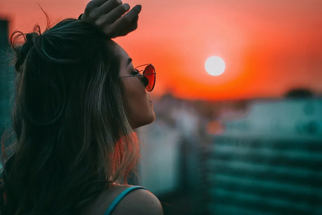 a girl looking up at the sun with her hand on her forehead