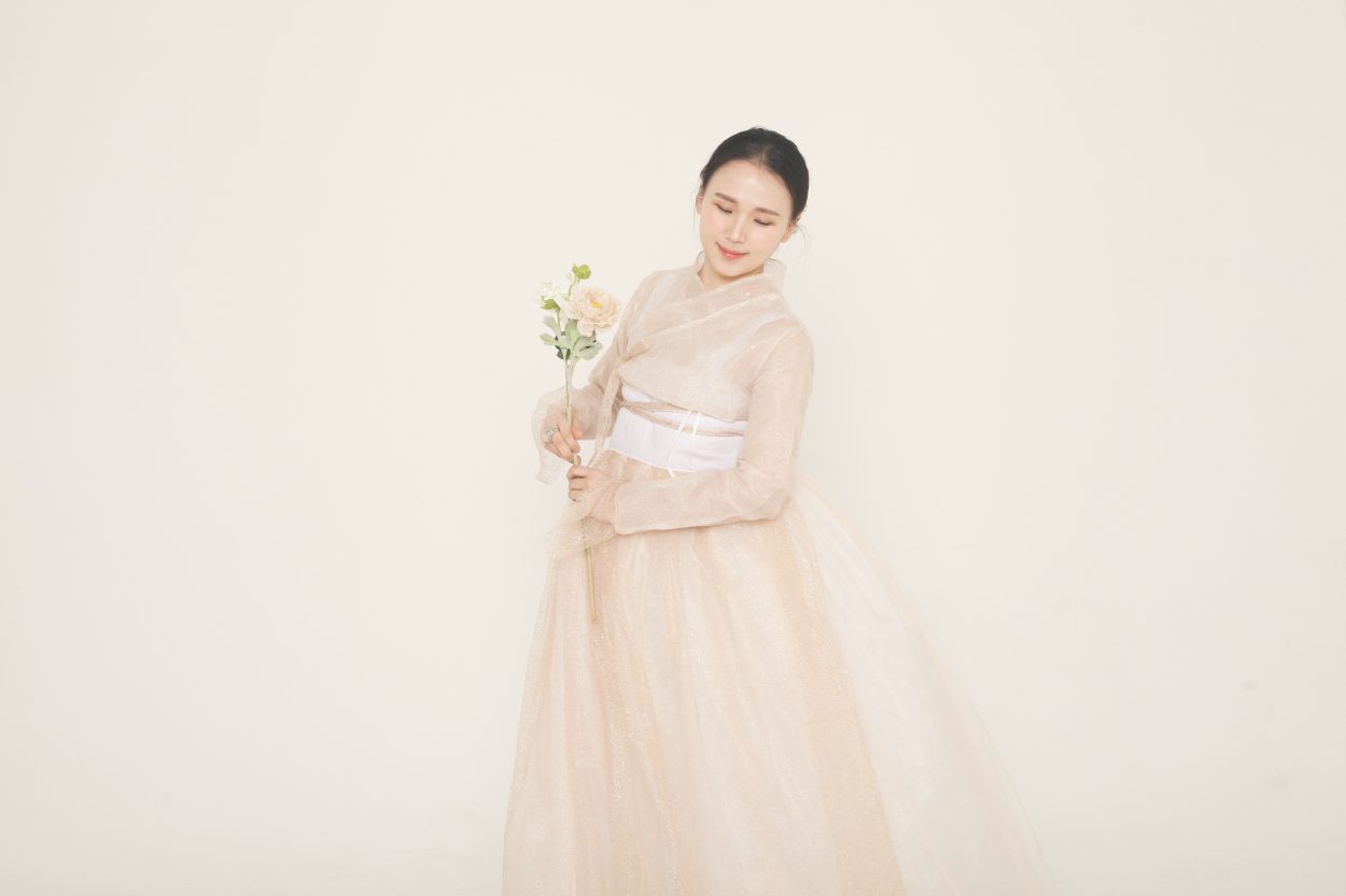 A woman posing in beige colored Korean traditional clothing holding a flower.