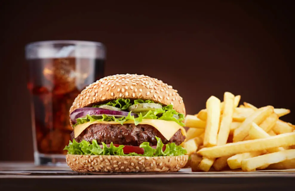A glass of cola with a beef burger and fries is set on a table.