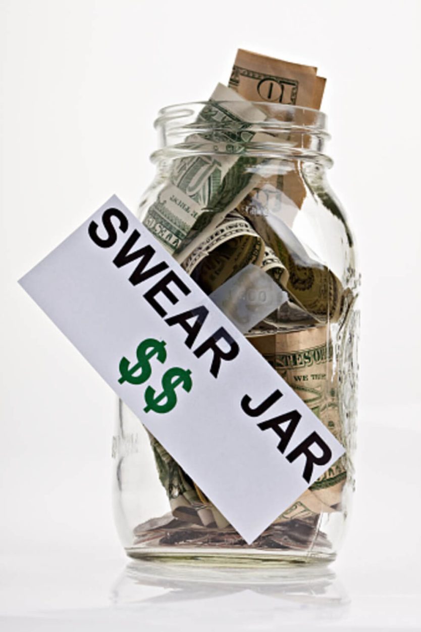 A photograph of a clear, crystal jar with money in it, and a swear written on the cardboard.