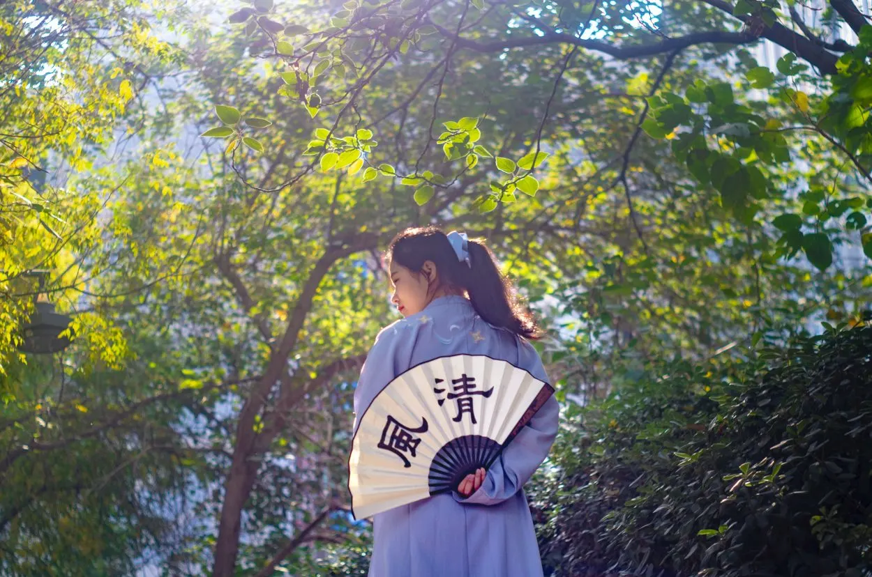 A girl dressed in traditional clothing of China holding a handheld fan