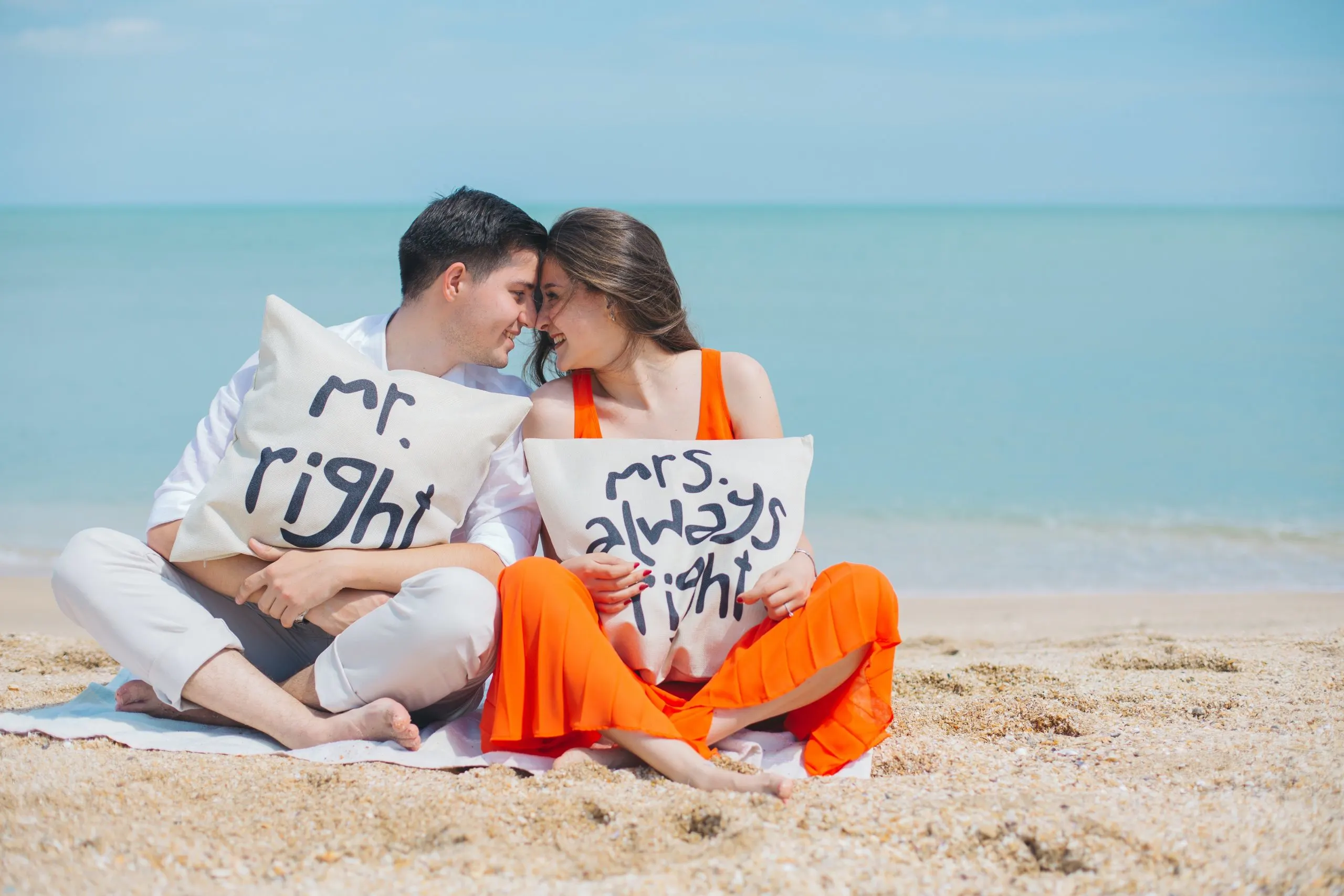 two people sitting on a beach with pillows