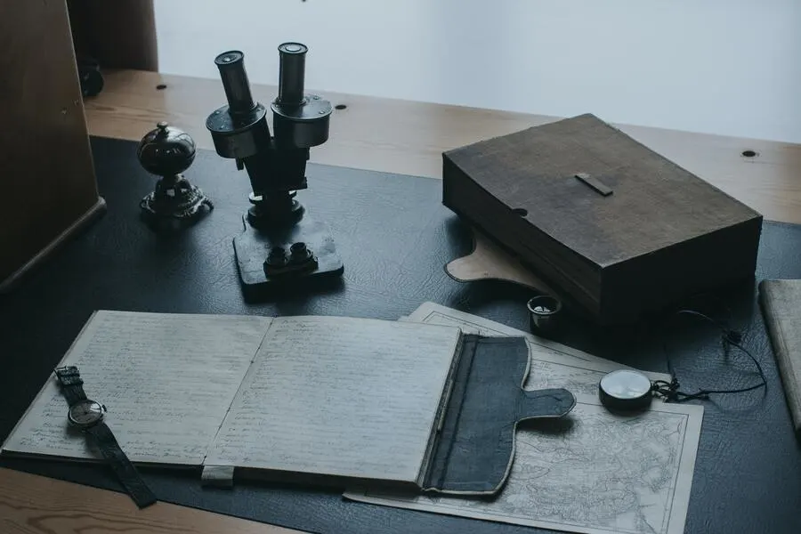 Multiple tools including a compass, a microscope, books and maps on a black wooden table. 