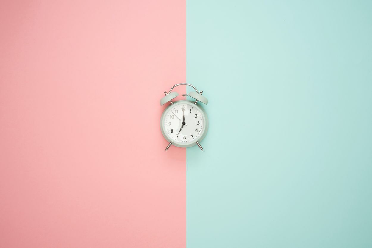 an alarm clock laying on a pink and blue backdrop