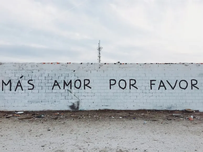 The words "but love please" is written in Spanish on a brick wall