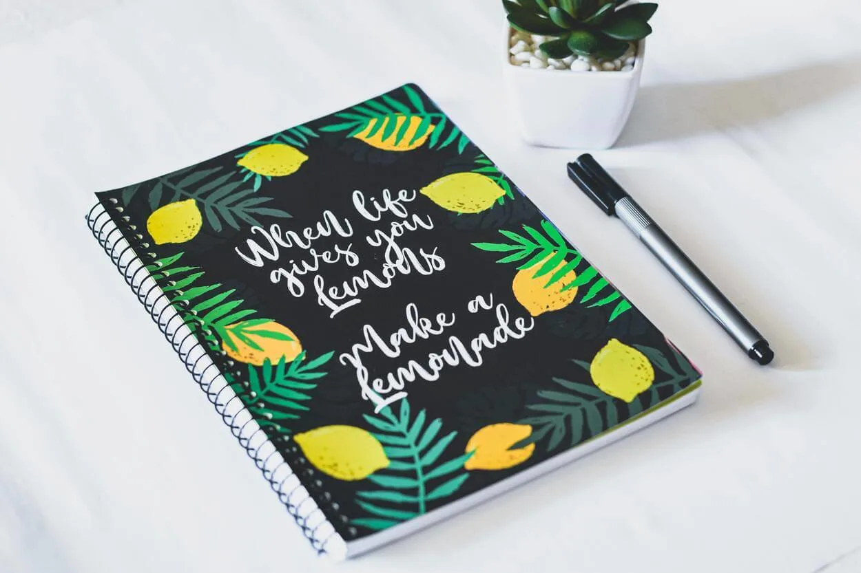 An image of a note book along with a pen with a motivational quote printed on it.