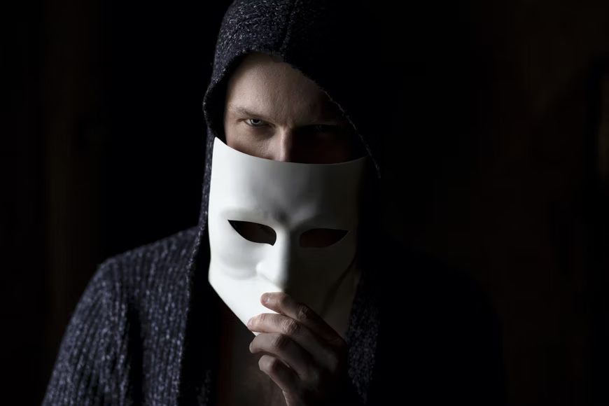 Person in black sweater with anonymous mask in hand