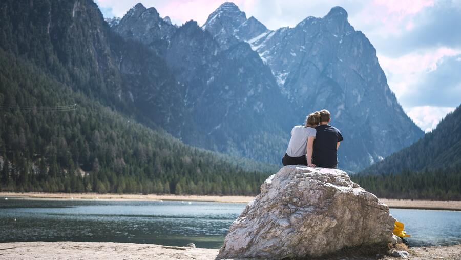 couple sitting on a rock in front of a lake together 