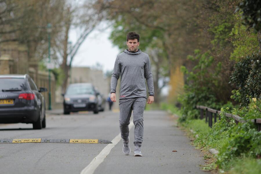 A picture of a man jogging while wearing a fitted pair of grey joggers and a hoodie.