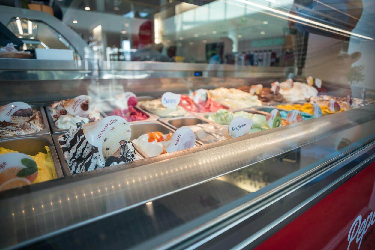 An image of a deep freezer with a glass top showing variety of ice cream flavors.