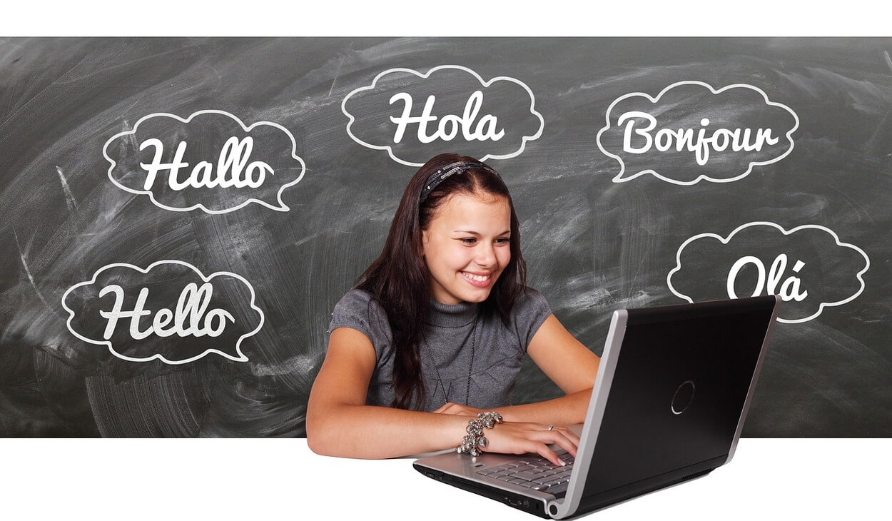 An image of a girl with a laptop and a black board showing the word hello in different languages.