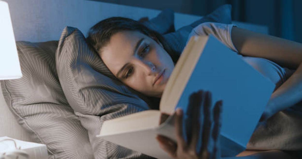 Woman relaxing in her bed and reading a book at night