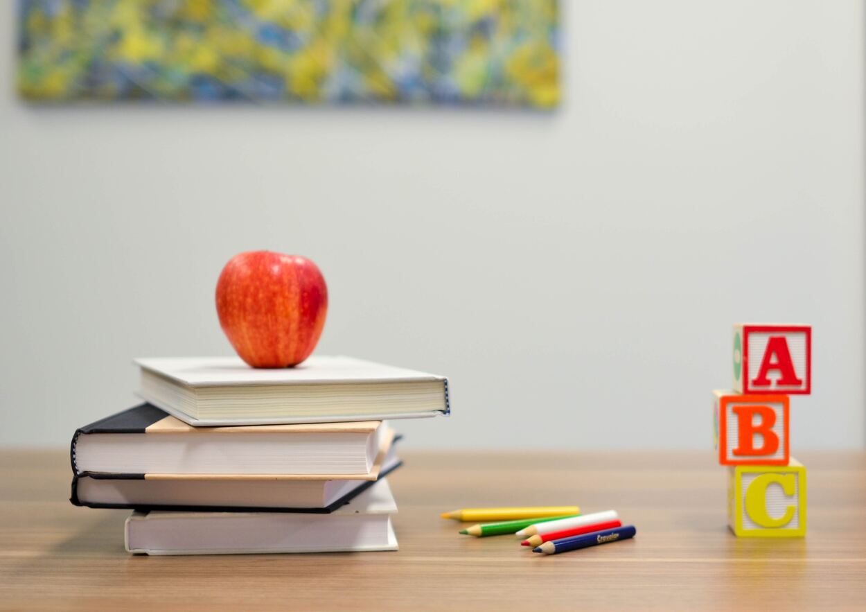 An apple on top of some books next to a pencil next to blocks of letters.