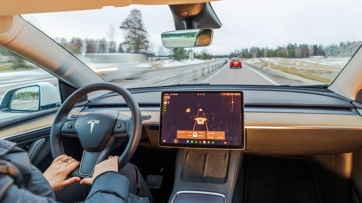 Interior of Tesla Model Y with driver using autopilot on highway through snowy winter landscape.