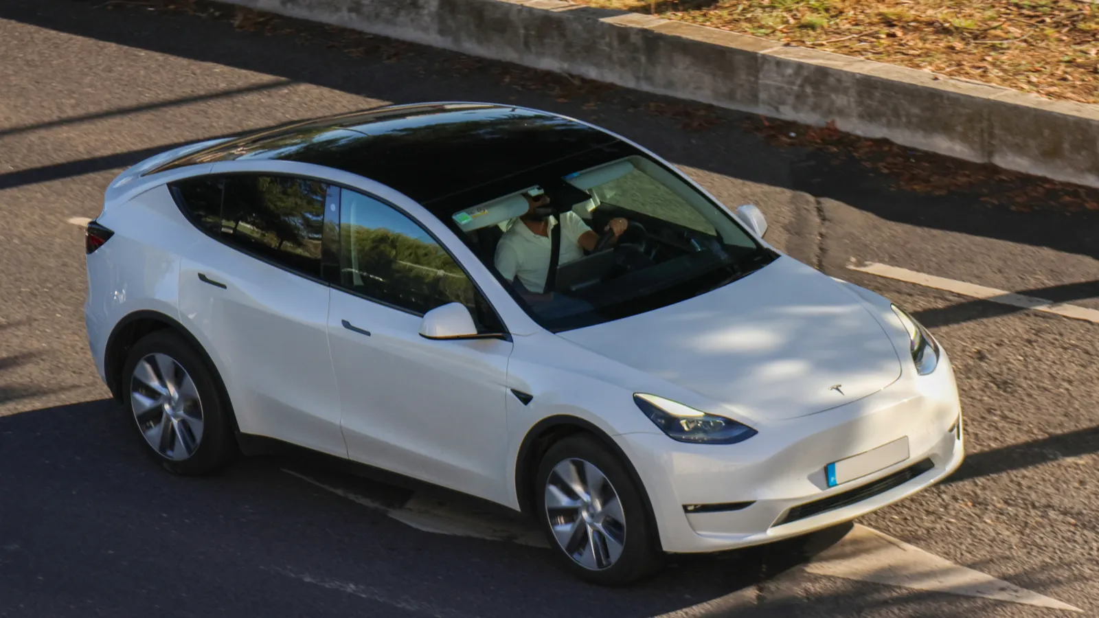 White tesla model y driving on a city street on a sunny day.