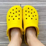 legs in bright yellow crocs footwear on the grey background